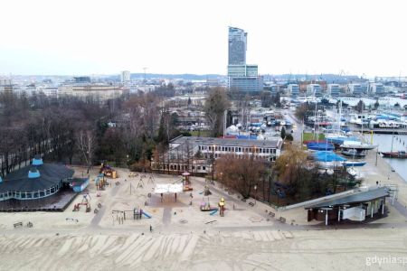 Zdjęcie plaży Gdynia Śródmieście z drona. na dole zdjęcia plaża i wymieniona kładki, na górnej części panorama Gdyni z Sea Towers
